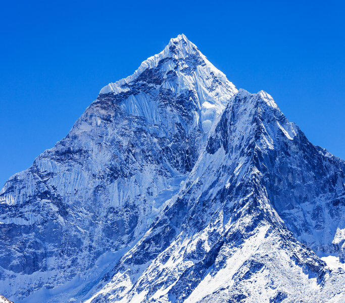 Craggy peak of a snowy mountain with bright blue sky background.