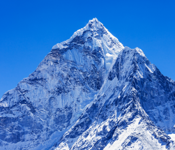 Craggy peak of a snowy mountain with bright blue sky background.