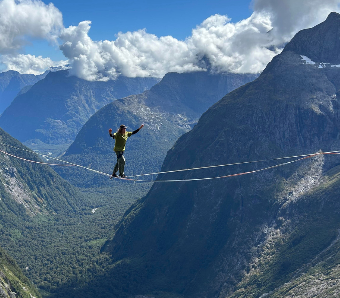 Man walking on a high line between two large mountains.