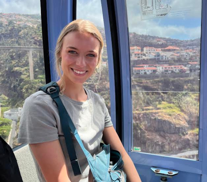 Erin Salisbury smiling, sitting in a gondola, wearing a gray t shirt and a blue shoulder bag.