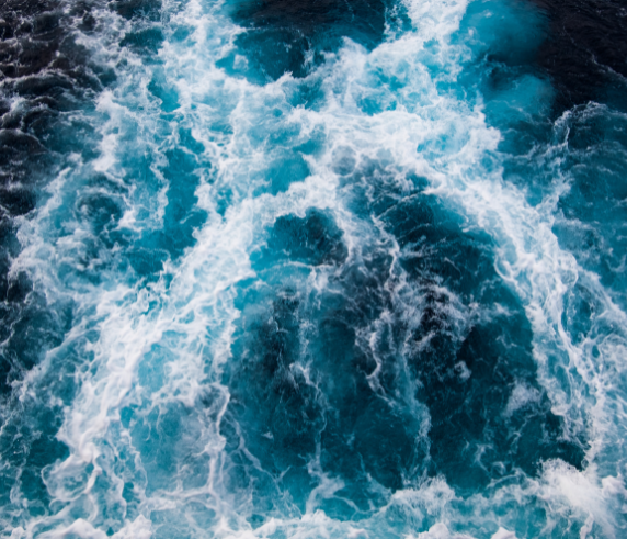 Bird's eye view of a churning ocean with white water and blue water.
