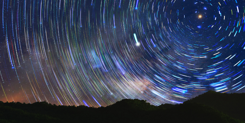 Night time long exposure photo of stars spinning in a circle. There is a black mountain range spanning the width of the photo at the bottom
