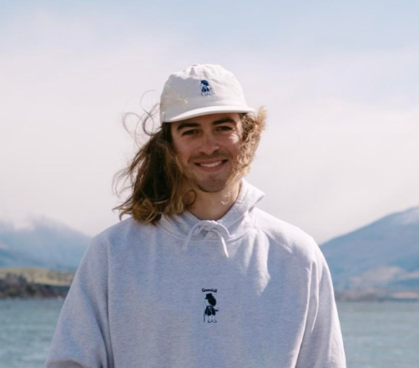 Henry, cofounder of Indigo Media Solutions, with a white hat and white sweatshirt on, standing in front of mountains and a lake